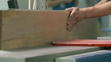 Close-up of man cutting board on machine. Creative. Carpenter processes wooden board on machine. Industrial processing and trimming of wooden boards with carpenters and machine tools video
