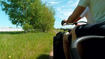 Riding a quad bike along the fields. Clip. Riding along the countryside path near forest and field on a cloudy sky background, active lifestyle. video