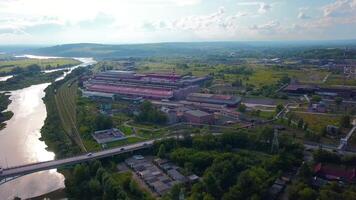 Top view of small factory town by river. Clip. Beautiful landscape with highway and river near town with factory in wooded area. Factory town by river with bridge in forest area in summer video