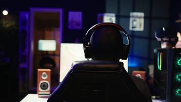 Man playing SF space videogame on PC screen in dark room wearing headphones, shooting asteroids. Gamer enjoying spaceship flying game on computer monitor, destroying meteorites, camera B video