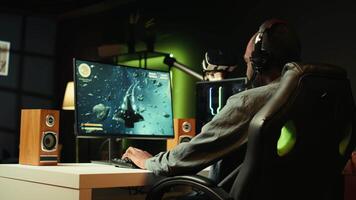 Man using headphones to enjoy online spaceship videogame with friends, shooting asteroids. Player discussing with teammates through headset microphone, flying in galaxy, camera B video