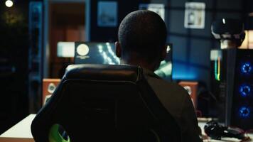 Man playing SF videogame on PC in neon illuminated apartment bedroom. Gamer enjoying spaceship flying game on computer display in RGB lit home late at night, camera B dolly out shot video