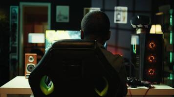 Man playing SF space videogame on PC screen in neon illuminated apartment living room. Gamer enjoying spaceship flying game on computer desktop display in RGB lit home late at night, camera B video