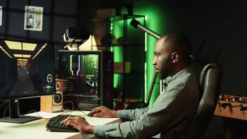 Portrait of smiling man playing FPS videogame on PC screen in neon illuminated apartment living room. Cheerful gamer enjoying shooter game on computer desktop display in RGB lit home, camera B video