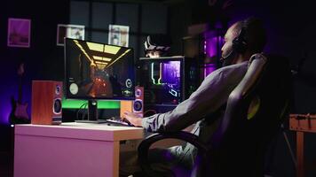 Man feeling happy while playing videogames on computer desktop with headphones on, celebrating victory. Cheerful gamer smiling after winning game on gaming PC while at home, camera B video