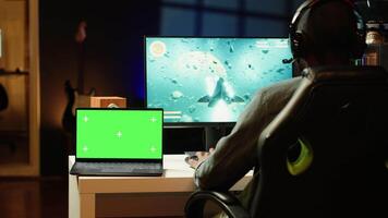 Mockup laptop on desk next to man playing SF videogame on computer, talking into headset with friends. Isolated screen notebook and gamer using headphones to chat with Esports team in game video