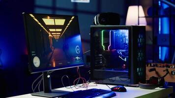 FPS videogame left open on PC screen in empty neon illuminated apartment living room. Shooter game on computer desktop display in RGB lit home late at night with no people in video