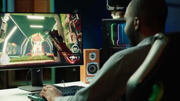 Professional gamer competing in intense online multiplayer videogame, streaming live from vibrant living room with neon lights. Man using PC, having immersive experience while gaming, camera A video