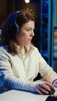 Vertical Freelancer editing professional photographs, working in home studio while enjoying music. Photo editor using headphones to listen favorite songs while using editing software, camera B video