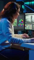 Vertical Videographer working on film montage, editing color grading and listening music. Post production studio worker manipulating raw footage, doing adjustments, wearing headphones, camera B video