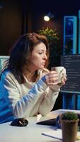 Vertical Portrait of happy computer engineer enjoying hot tea while implementing security measures to protect company systems and data. Joyful IT worker holding coffee mug and debugging code, camera B video