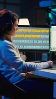 Vertical Photographer using editing software to edit photos and make adjustments while enjoying cup of coffee. Specialist color correcting pictures while listening music in headphones, camera B video