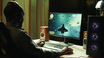Gamer in neon lit apartment home shooting meteorites in spaceship flying singleplayer game on computer desktop. Player navigating galaxy, exploding enemies in simulation game on gaming PC, camera B video