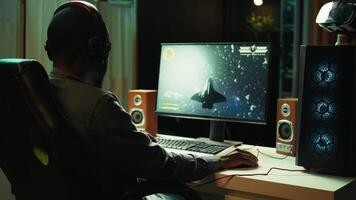 African american man wearing headphones playing SF space videogame on PC screen in blurry background, shooting lasers. Close up of person enjoying galaxy flying game on computer monitor, camera B video