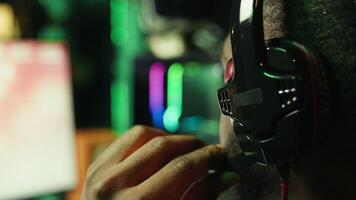Man playing SF videogame on computer, having fun in neon lit apartment, close up. Gamer competing in online multiplayer game, using headphones to talk with teammates, camera B video