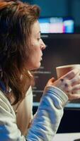 Vertical Portrait of happy computer engineer enjoying hot tea while implementing security measures to protect company systems and data. Joyful IT worker holding coffee mug and debugging code, camera A video