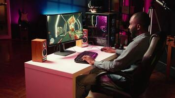Man having fun by playing videogames on gaming PC at computer desk, enjoying day off from work. Gamer battling enemies in online multiplayer shooter from the comfort of his home, camera B video