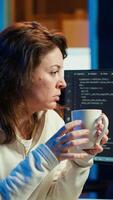 vertical retrato do sorridente isto especialista bebendo café enquanto olhando para companhia segurança vulnerabilidades e impedindo malware infecções. programador desfrutando quente bebida enquanto escrevendo código, Câmera uma video