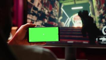 Man watching favorite content creator on isolated screen smartphone showing tips for game he is currently playing. Player looking online for inspiration on mockup phone, stuck on mission video