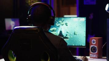 Man using headphones to enjoy online spaceship videogame with friends, shooting asteroids. Player discussing with teammates through headset microphone, flying in galaxy, camera A video