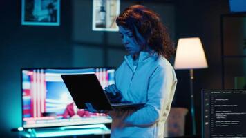 Woman walking in apartment designing and developing software applications using laptop. IT professional standing in living room, implementing and maintaining company systems, camera A video