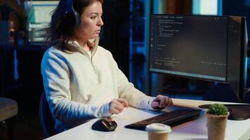 Woman listening music while doing software quality assurance, reading source code on computer screen. Developer wearing headphones enjoying podcasts and inspecting coding on desktop PC, camera A video
