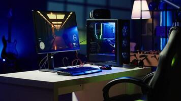 Empty apartment living room with neon lights and gaming computer with first person shooter game left open on monitor. Singleplayer videogame on desktop pc display on desk late at night video
