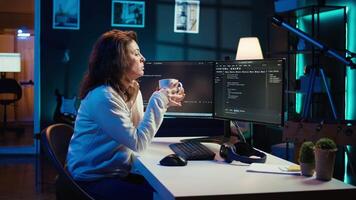 Portrait of smiling IT specialist drinking coffee while looking for company security vulnerabilities and preventing malware infections. Programmer enjoying hot beverage while writing code, camera B video