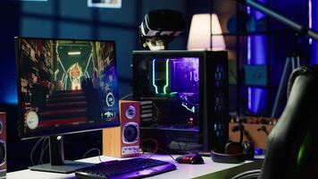 Computer screen showing FPS videogame left open at night in empty apartment with RGB lights. Close up shot of PC, keyboard and mouse on desk in living room with no people in video