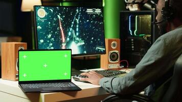 Isolated screen laptop next to professional streamer competing in online multiplayer videogame, streaming live at home. Mockup notebook and man playing on PC, using headphones to talk with audience video
