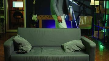 Fatigued player in RGB lit home late at night gaming with gamepad. Sleepy person sitting on sofa in neon illuminated apartment, playing videogames on console, looking exhausted, camera B video