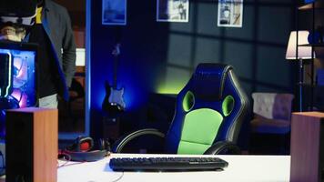 POV of happy man entering room, playing FPS videogame on PC screen in neon illuminated apartment living room. Joyous gamer coming home to enjoy game on computer in RGB lit house, camera B video
