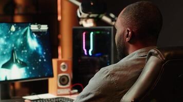 Gamer in neon lit apartment home shooting meteorites in spaceship flying singleplayer game on computer desktop. Player navigating galaxy, exploding enemies in simulation game on gaming PC, camera A video