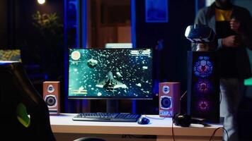 Man playing SF space videogame on PC screen in neon illuminated apartment living room. Gamer enjoying spaceship flying game on computer desktop display in RGB lit home late at night, camera A video