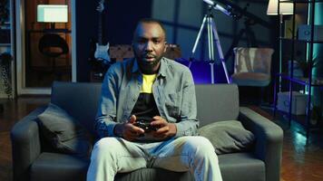 Gamer on couch celebrating winning esports videogame tournament, playing with friends online. Player rejoicing after gaming championship victory, enjoying multiplayer game with teammates, camera B video