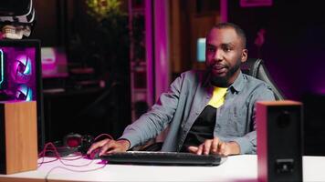 Man in neon lit apartment playing intense videogames on gaming PC at computer desk. Gamer competing against enemies during internet multiplayer competition, unwinding at home, camera A video