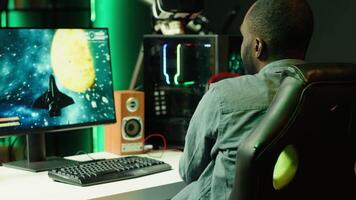 Man playing SF shooter videogame on computer monitor, talking into headset with friends. Gamer using headphones while enjoying game with spaceship flying to chat with Esports team, camera A video