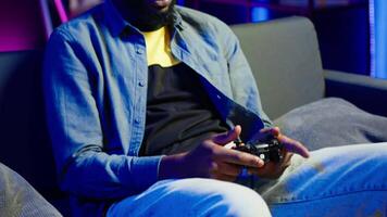 Gamer on couch using controller and headphones to play videogame at home, close up. Man in home theatre using high tech gaming console gamepad to defeat opponents in game, camera A video