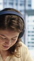 Vertical Business entrepreneur enjoys working with music on her headset, solving daily tasks at her corporate office. Determined powerful female CEO having fun with favorite songs, productivity. Camera A. video
