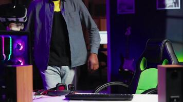 POV of happy man entering room, playing FPS videogame on PC screen in neon illuminated apartment living room. Joyous gamer coming home to enjoy game on computer in RGB lit house, camera A video