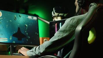 African american man wearing headphones playing SF space videogame on PC screen in blurry background, shooting lasers. Close up of person enjoying galaxy flying game on computer monitor, camera A video
