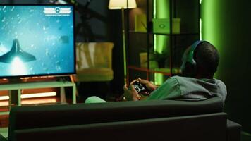Man playing entertaining spaceship flying videogame on large smart TV, wearing headphones. Player enjoying SF arcade game on gaming console, piloting spacecraft in galaxy using gamepad, camera A video