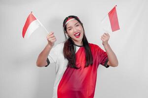 Excited young Indonesian woman wearing jersey is holding flags watching sport match competition. photo