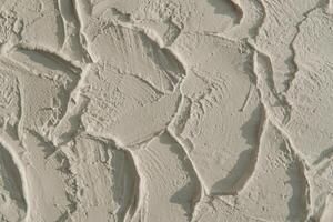 Photography of a wall covered in white paint or cement with a textured, uneven surface. photo