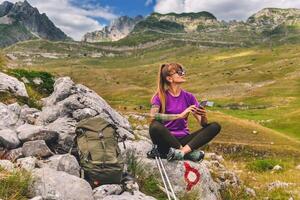 Female Hiker with Backpack Sitting on Rock Using Smartphone photo