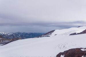 view of the high mountains above the clouds from the glacier on the slope of Mount Elbrus photo