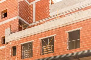 Detailed view of a building under construction, showcasing red brick walls with unfinished openings and supporting beams, highlighting the ongoing architectural process. photo