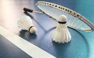 Cream white badminton shuttlecock and racket with neon light shading on dark floor in indoor badminton court, copy space, soft and selective focus. photo