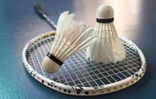 Cream white badminton shuttlecock and racket with neon light shading on dark floor in indoor badminton court, copy space, soft and selective focus. photo