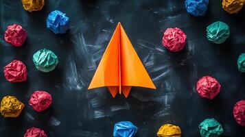 An orange paper airplane surrounded by colorful crumpled paper photo